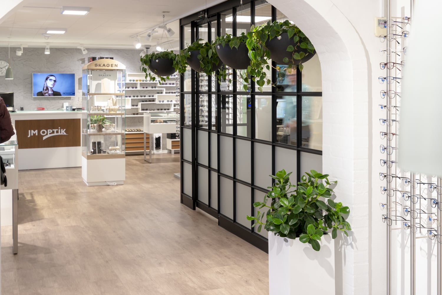 Svart ampel med kedja monterad på vägg i butiksmiljö med gröna växter