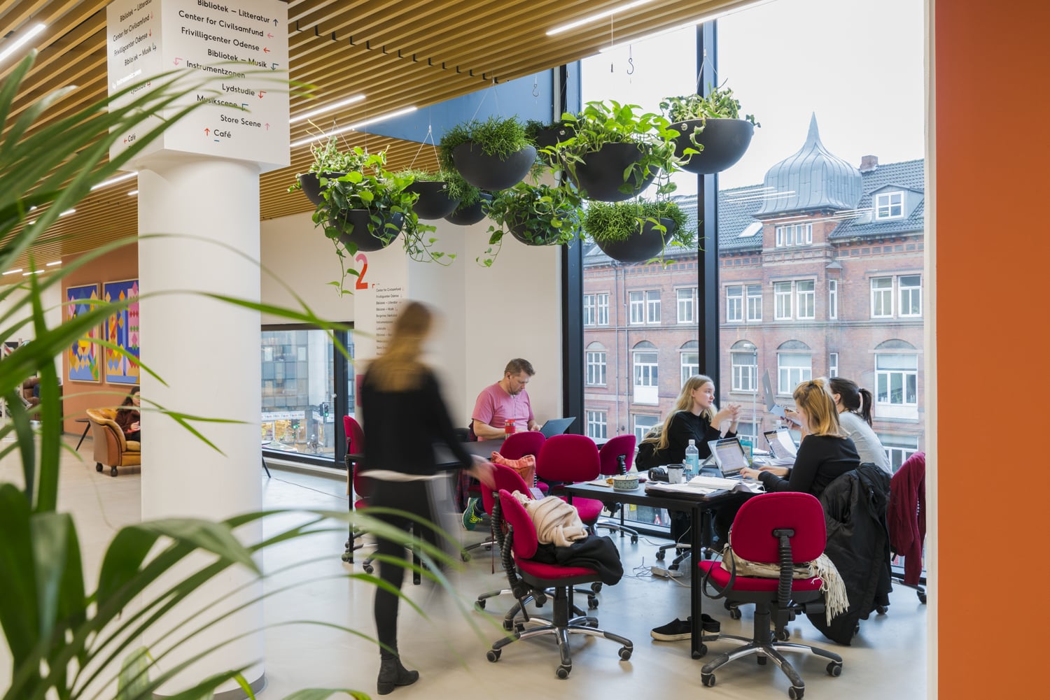 Hanging ampel med grönväxter i modernt kontorsmiljö med människor och stadsvyutsikt