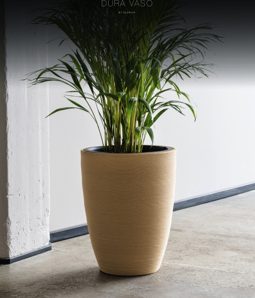 DURA VASO kruka i naturlig färg med lång gräsväxt, placerad på betongklinker mot vit vägg
