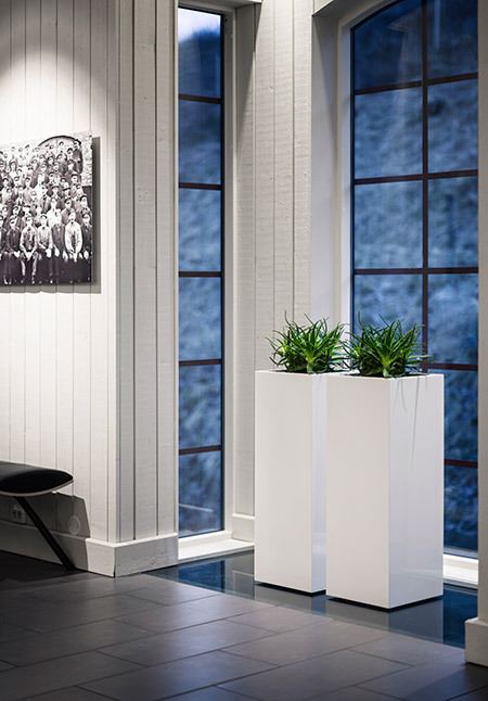 Två vita kvadratiska höga blomkrukor med hjul i modern inredning vid fönster med växter